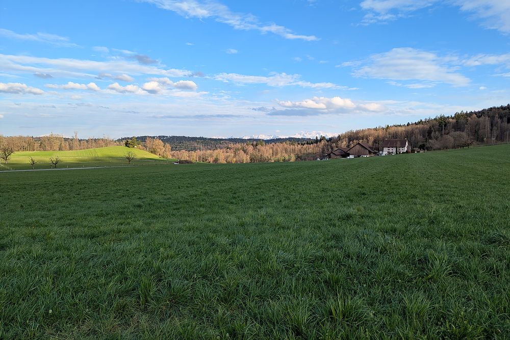 Open green meadows under a wide blue sky above the village.